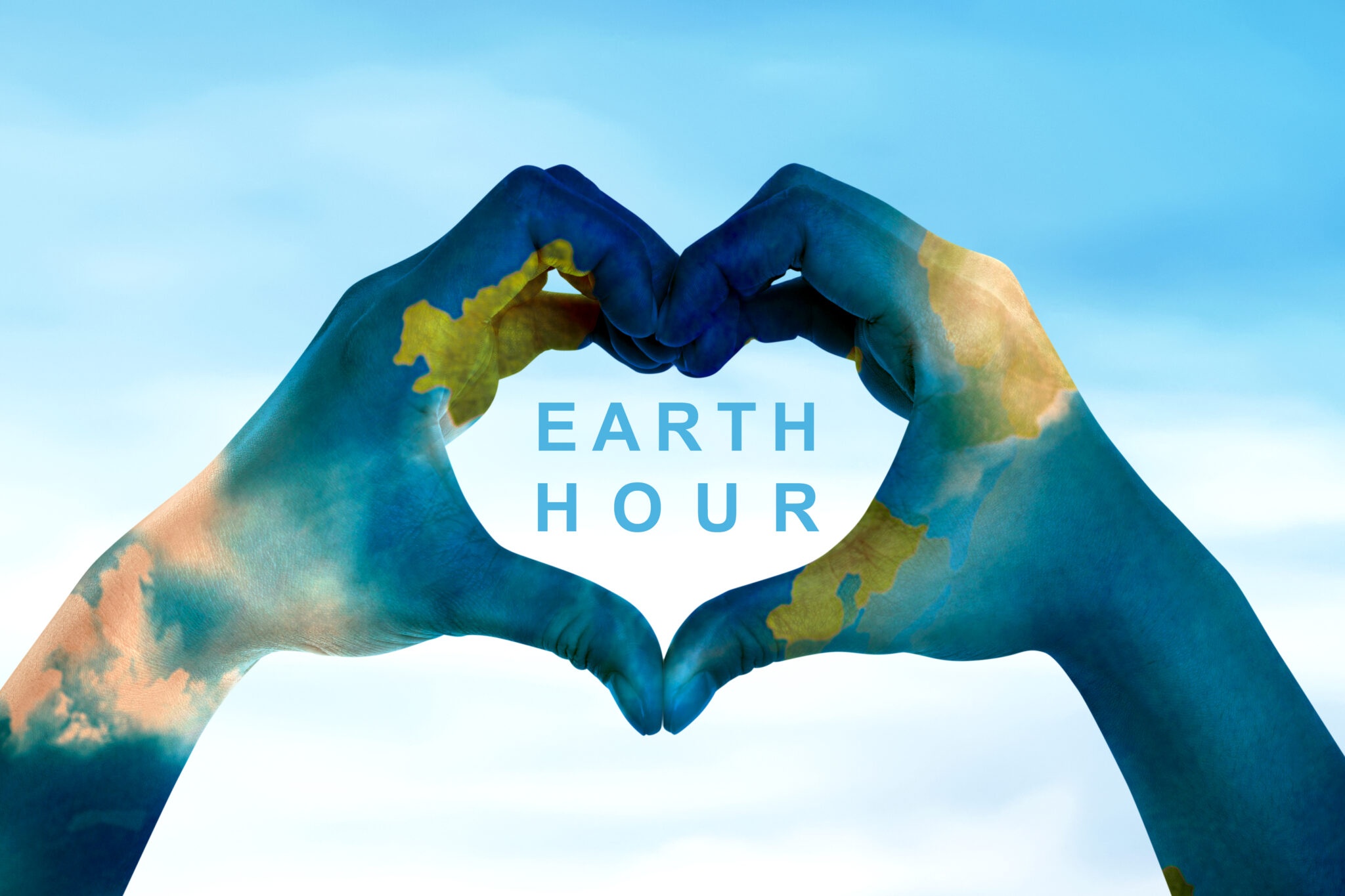 Human hands with world map skin make a heart shape with earth hour text over blue sky background. Earth hour concept.