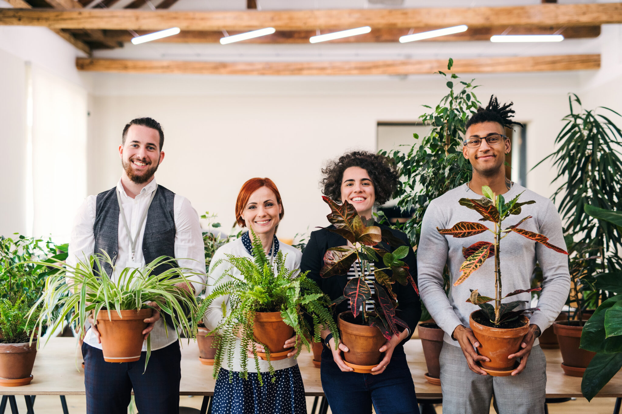 Group of young businesspeople standing in office, holding plants.