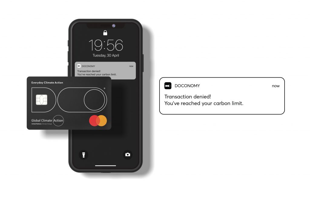 Image of DO Black credit card from Doconomy in full colour landscape orientation. Card is mocked half overlapping an iPhone, which sits in the background. Notification from Doconomy on iPhone screen reads "Transaction denied! You've reached your carbon limit."