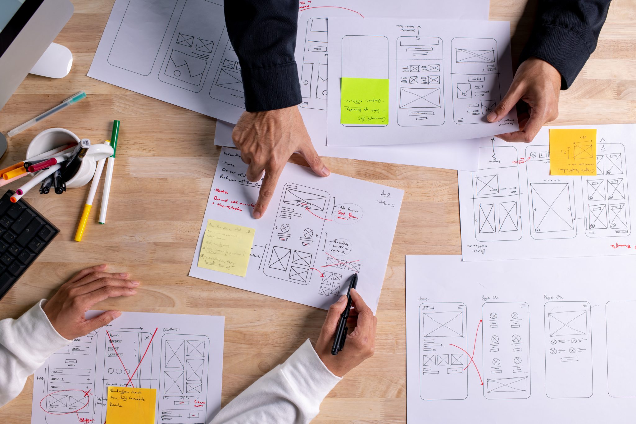 Hands of a design team working on UX wireframes and interface plans, illustrating efficient digital design processes.